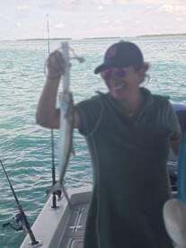 Angler proudly displaying a fish while fishing on a boat in clear waters.
