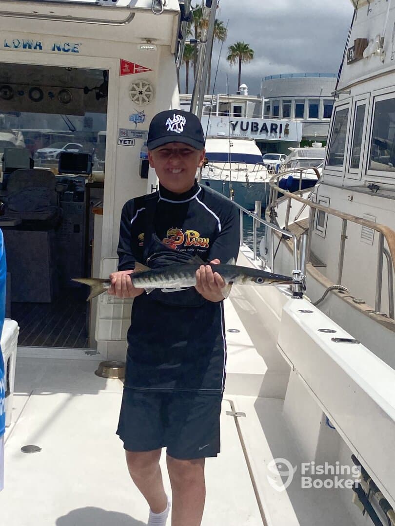 Young angler proudly holding a Barracuda on a fishing charter, showcasing a successful day on the water.