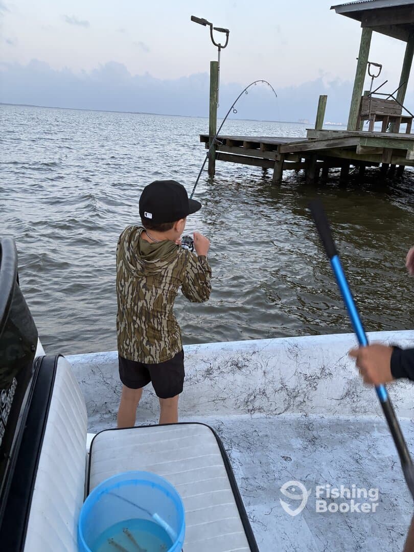 A young angler is reeling in a catch from the boat, showcasing the excitement of fishing in a coastal environment.