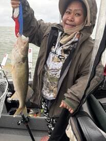 A proud angler holding a Walleye while fishing on a boat, showcasing a successful catch in a freshwater environment.