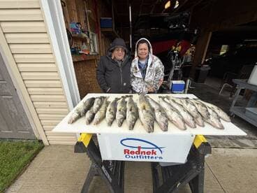 Two anglers proudly displaying a catch of Walleye on a board in a garage setting, showcasing their successful fishing trip.