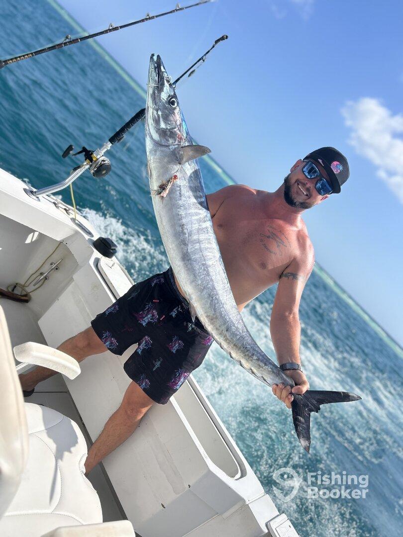 Angler proudly displaying a large Barracuda while aboard a fishing boat in clear blue waters.