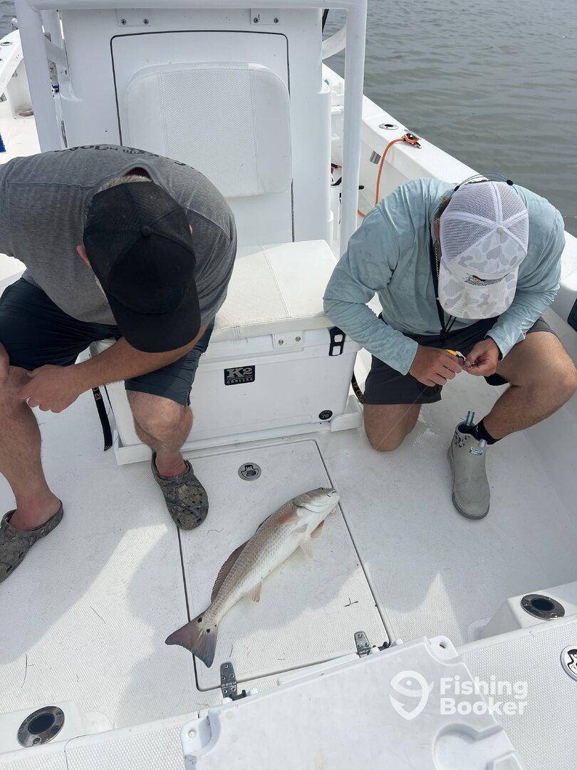 Two anglers examining a freshly caught Redfish on the deck of a fishing boat, showcasing the day's catch.