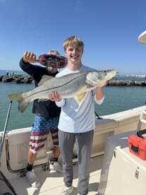 A young angler proudly displaying a large Snook while fishing with a guide on a sunny day.