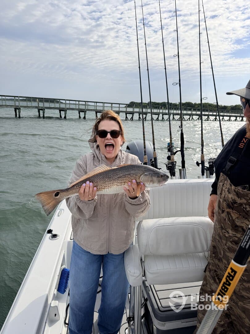 Excited angler holding a large Redfish on a boat, showcasing a successful fishing trip.