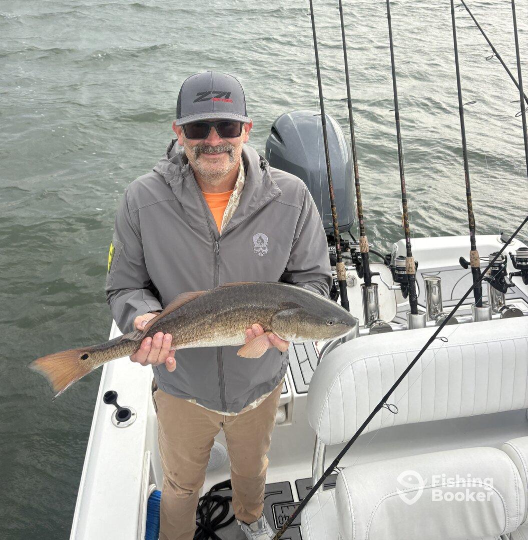 Angler proudly displaying a Redfish on a boat, showcasing a successful fishing trip.
