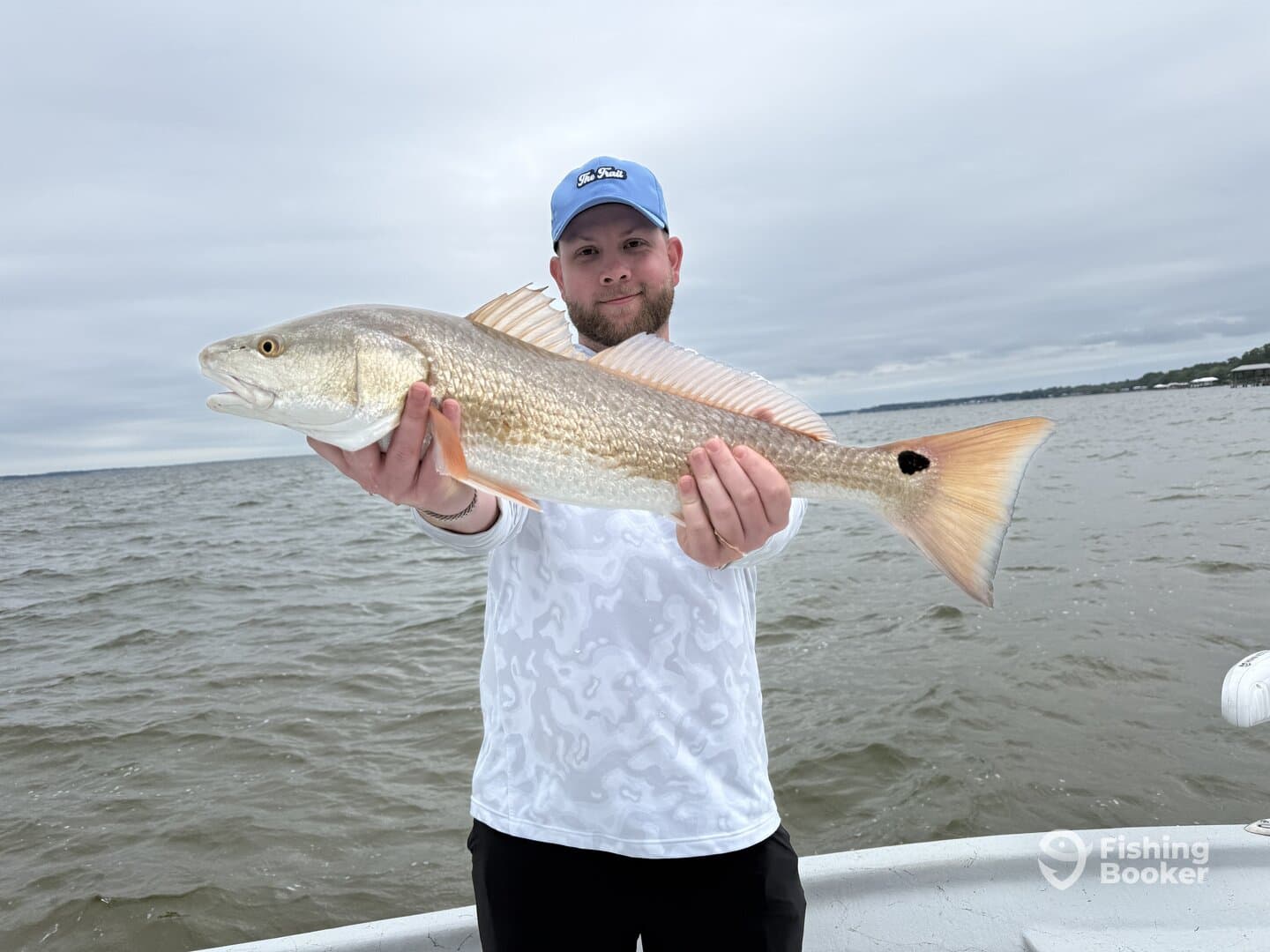 Angler proudly displaying a large Redfish while fishing on a cloudy day.