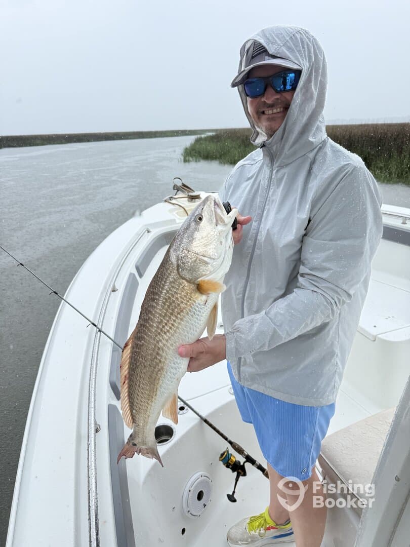 Angler proudly displaying a large Redfish while fishing in a rain-soaked marsh environment.