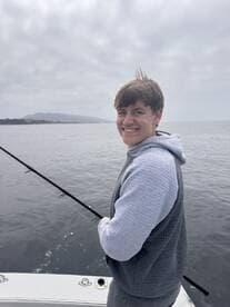 A young angler is actively fishing from a boat, enjoying a day on the water with a scenic backdrop.