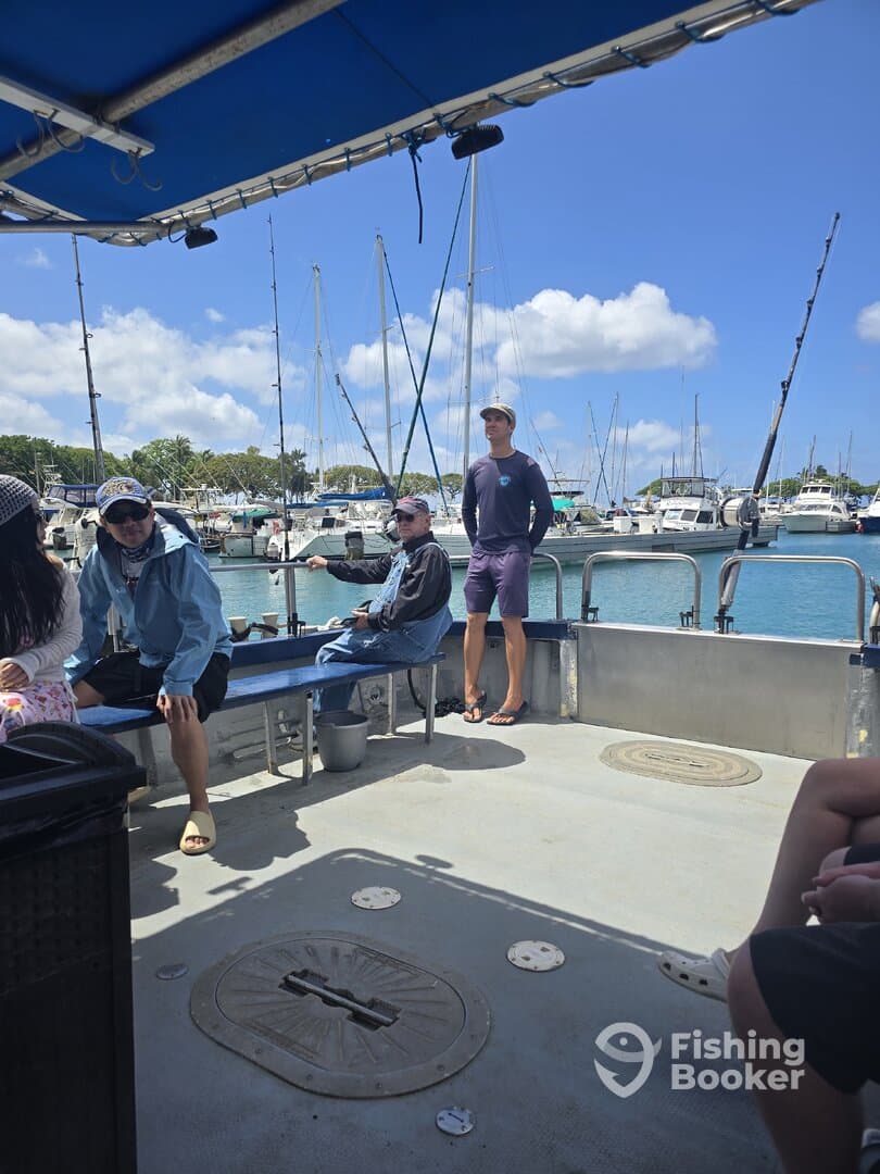 Passengers relaxing inside a fishing charter boat, with a view of the marina and fishing rods in the background.