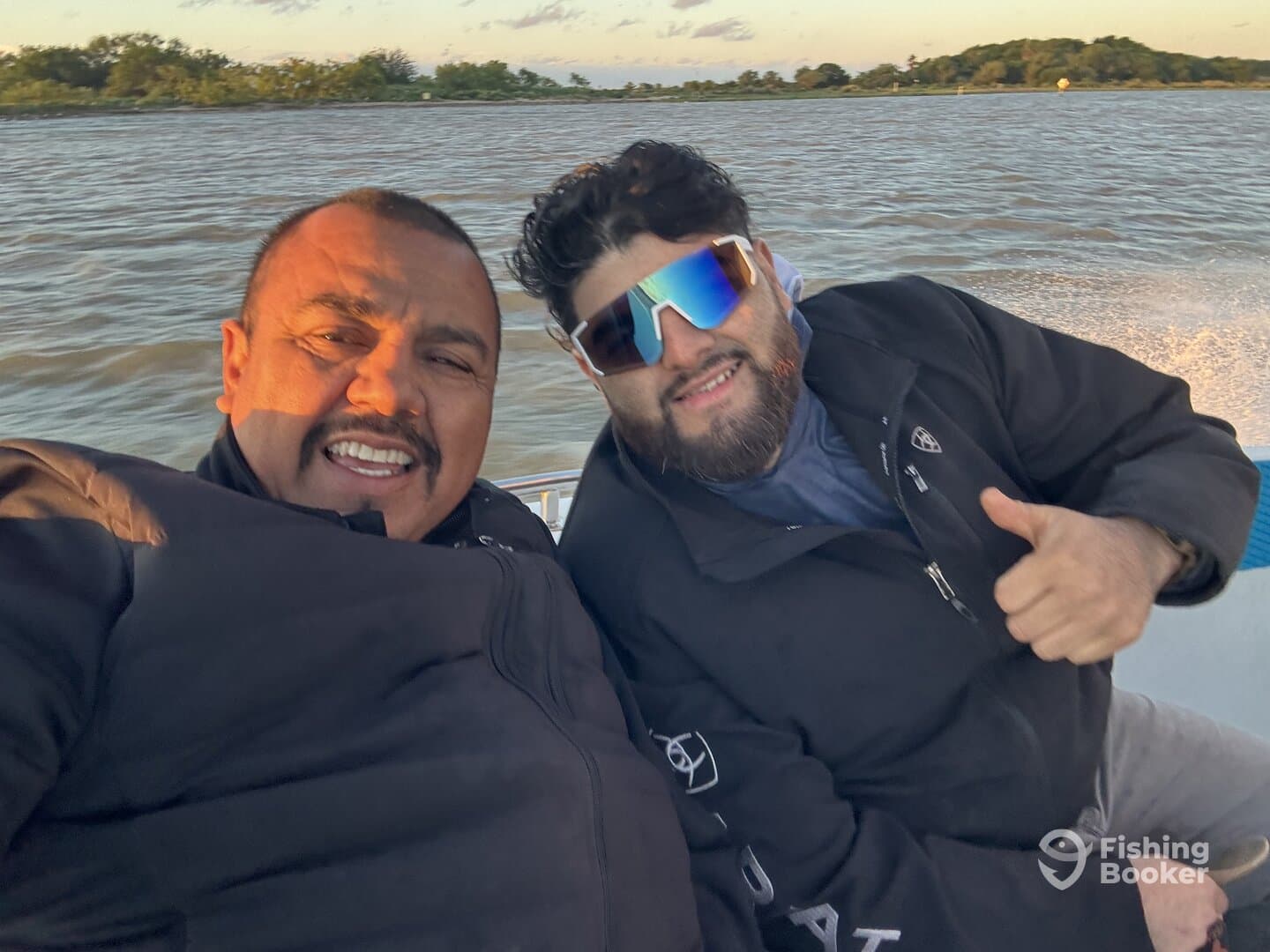 Two anglers enjoying a boat ride, smiling and posing for a selfie on a scenic waterway.
