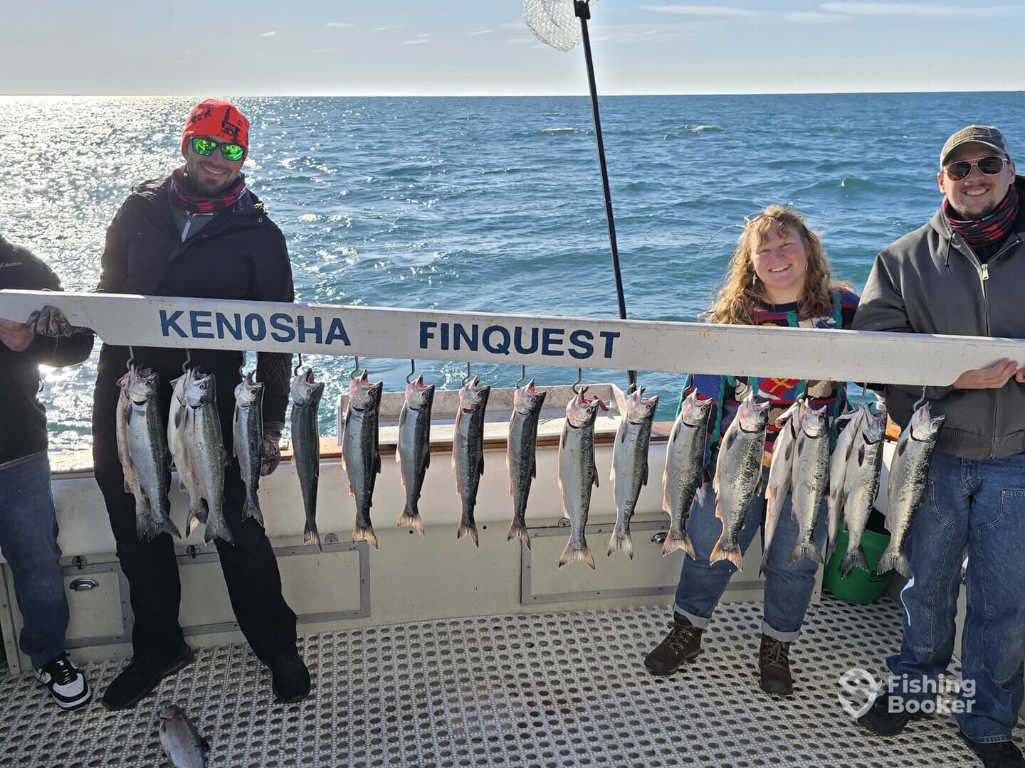 A group of anglers proudly displaying their catch of salmon on a board aboard the Kenosha Finquest, showcasing a successful fishing trip.