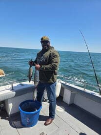 Angler proudly displaying two freshly caught fish while aboard a fishing boat, enjoying a sunny day on the water.