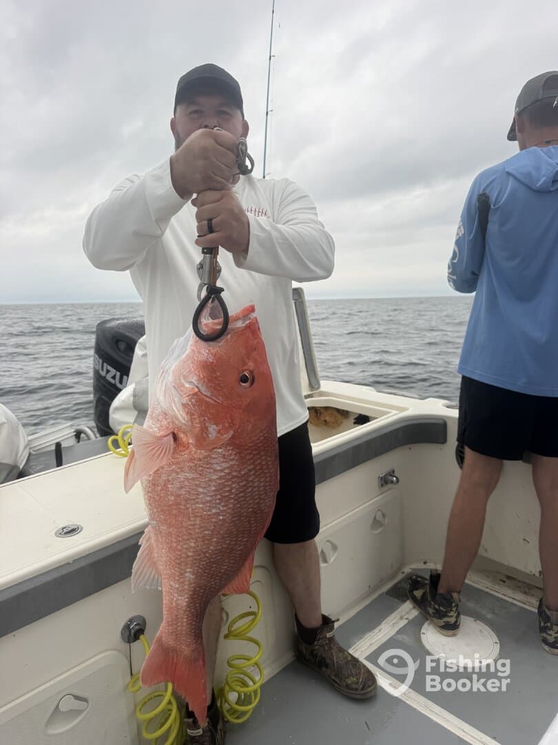 Angler proudly displaying a large Red Snapper while fishing offshore, with fellow anglers in the background.