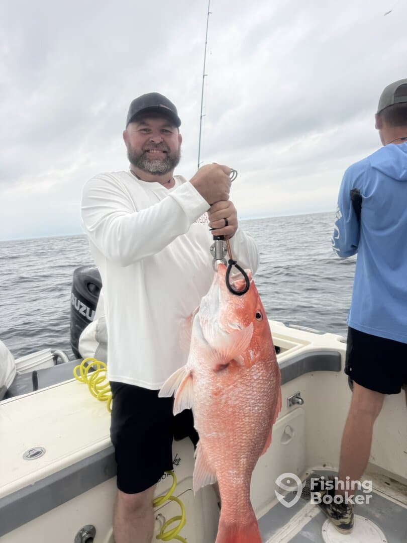 Angler proudly displaying a large Red Snapper while fishing offshore, showcasing a successful day on the water.