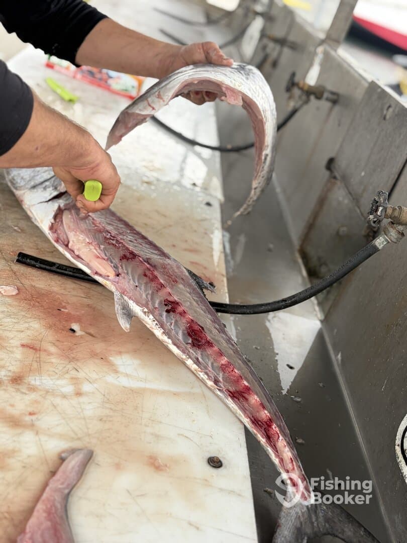 A fisherman skillfully filleting a freshly caught fish at a cleaning station, showcasing the detailed process of preparing the catch.
