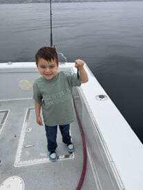 A young angler proudly displaying a small catch while fishing on a boat, showcasing a fun family fishing experience.