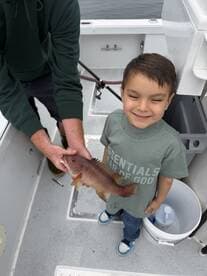 A young angler proudly holding a colorful fish on a boat, showcasing a memorable fishing experience.