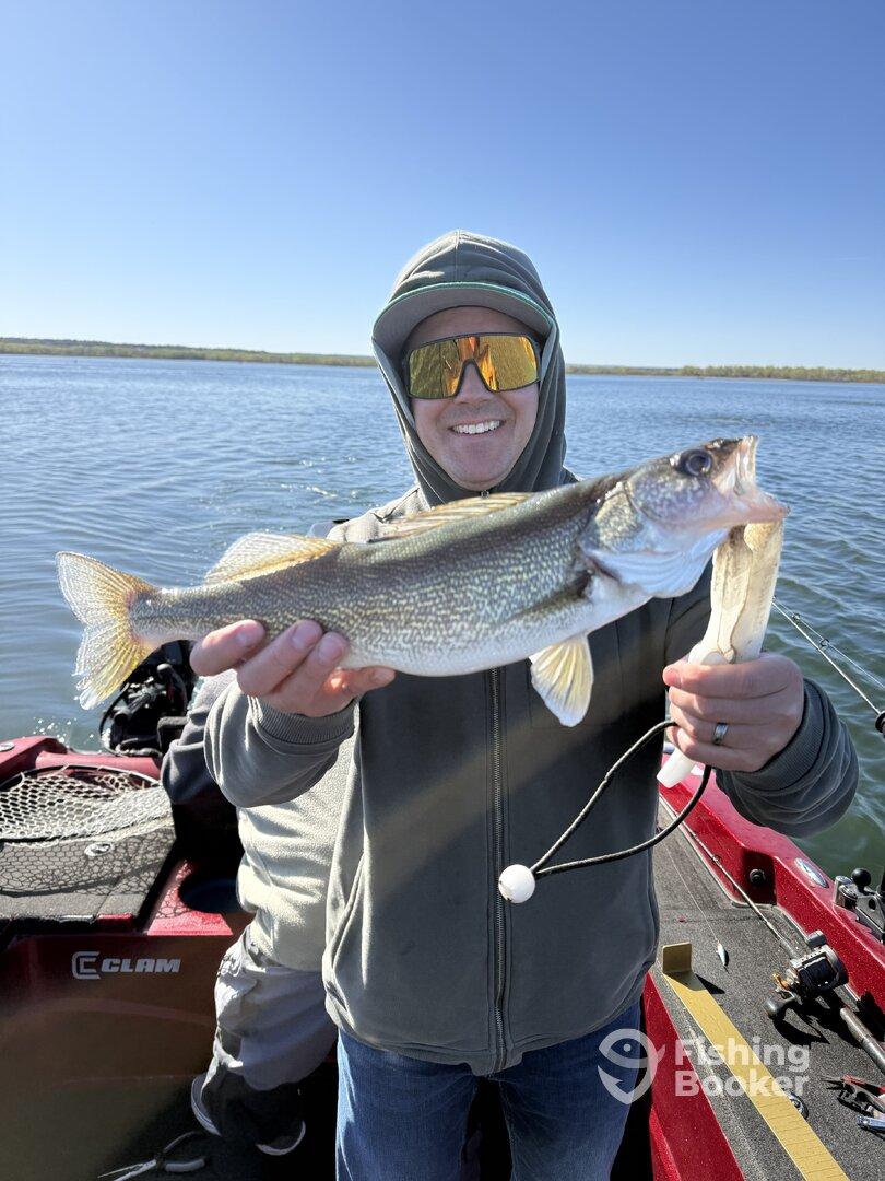 A happy angler proudly displaying a large Walleye while fishing from a boat on a clear day.