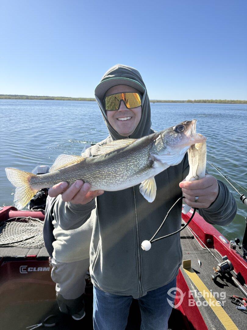 Angler proudly displaying a Walleye while fishing on a boat in a scenic lake setting.