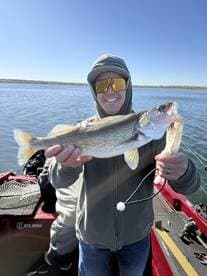 A happy angler proudly displaying a large Walleye while fishing from a boat on a clear day.