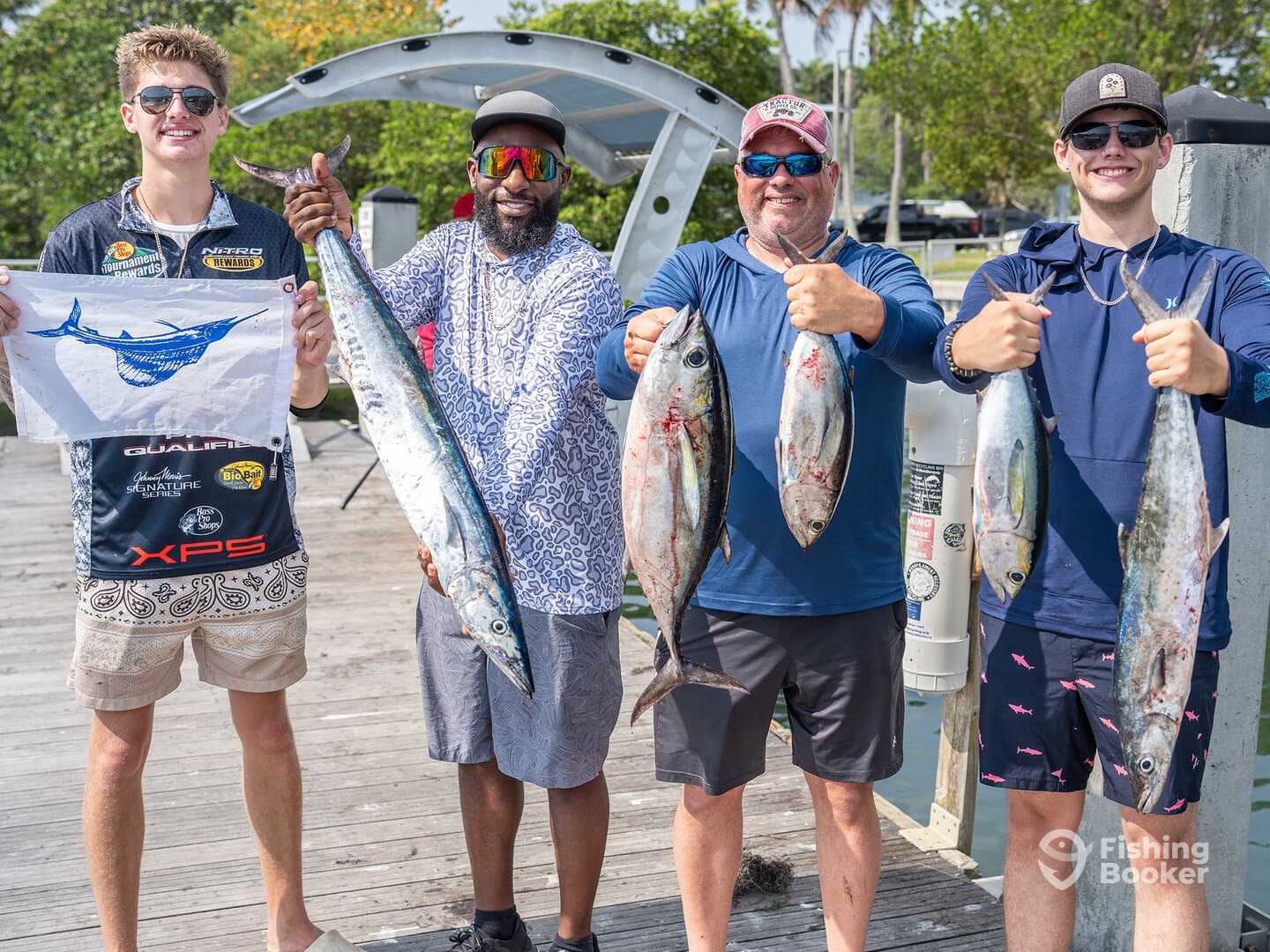 A group of anglers proudly displaying their catch, including a large Kingfish and several smaller fish, at the dock after a successful fishing trip.