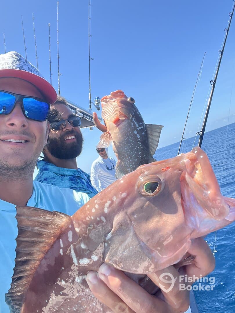 Anglers proudly displaying their catch, including a large Red Grouper, while fishing on a sunny day.