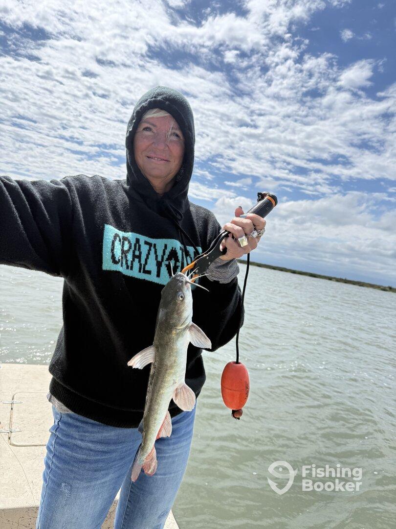 A proud angler holding a freshly caught catfish while standing on a dock, showcasing a successful fishing trip.