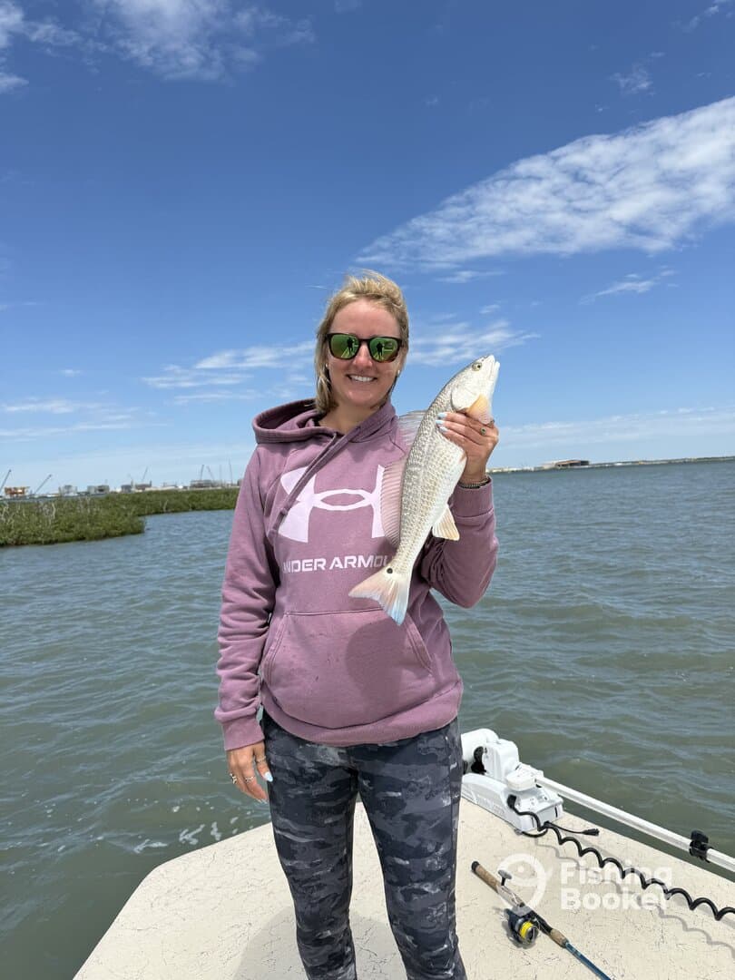 Angler proudly displaying a large Speckled Trout while fishing on a boat in a coastal waterway.