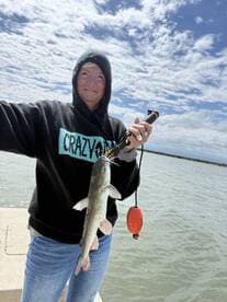 A proud angler holding a freshly caught catfish while standing on a dock, showcasing a successful fishing trip.