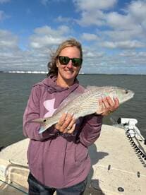 Angler proudly displaying a Redfish while on a boat, enjoying a sunny day on the water.