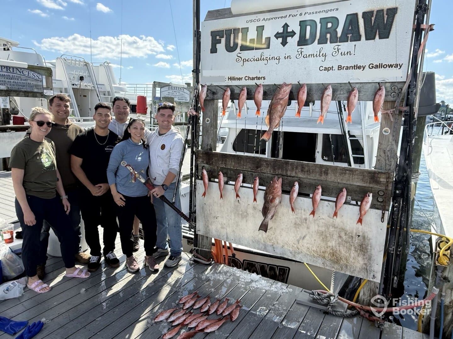 A group of six anglers proudly posing in front of a catch board displaying an array of Snapper after a successful fishing trip.