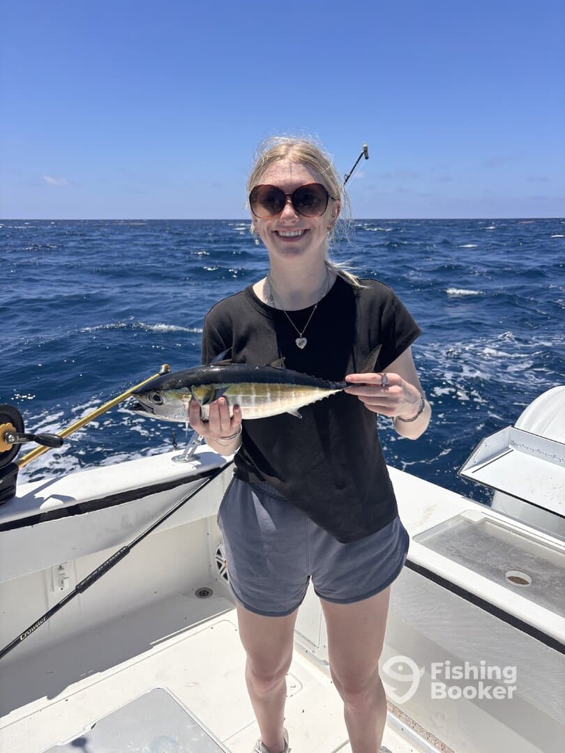 A young woman proudly displaying her catch, a small fish, while fishing on a boat in open waters.