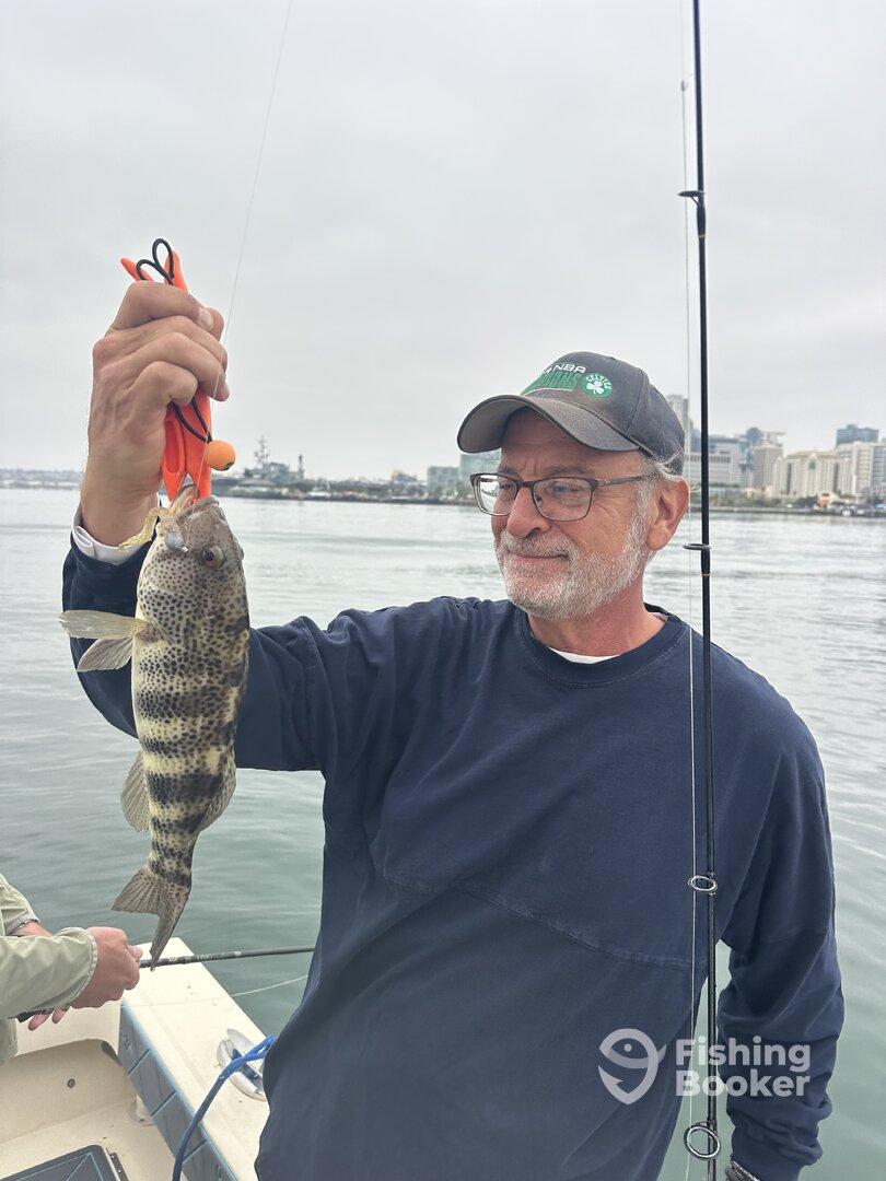 An angler proudly displaying a Spotted Bass while fishing from a boat in a coastal setting.