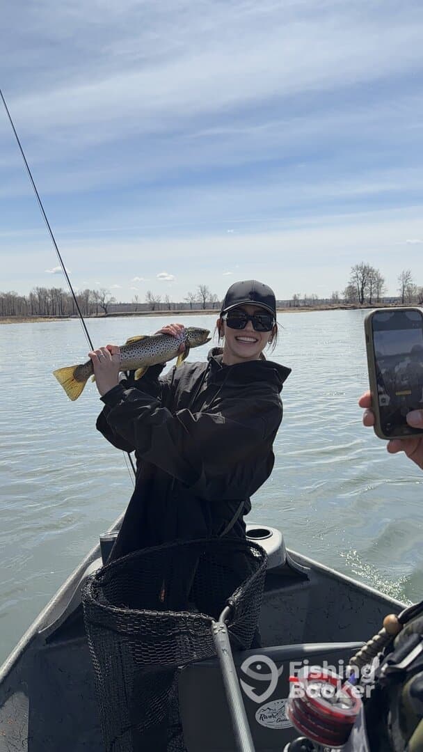 Angler proudly displaying a large trout while fishing on a river, capturing a joyful moment with friends.