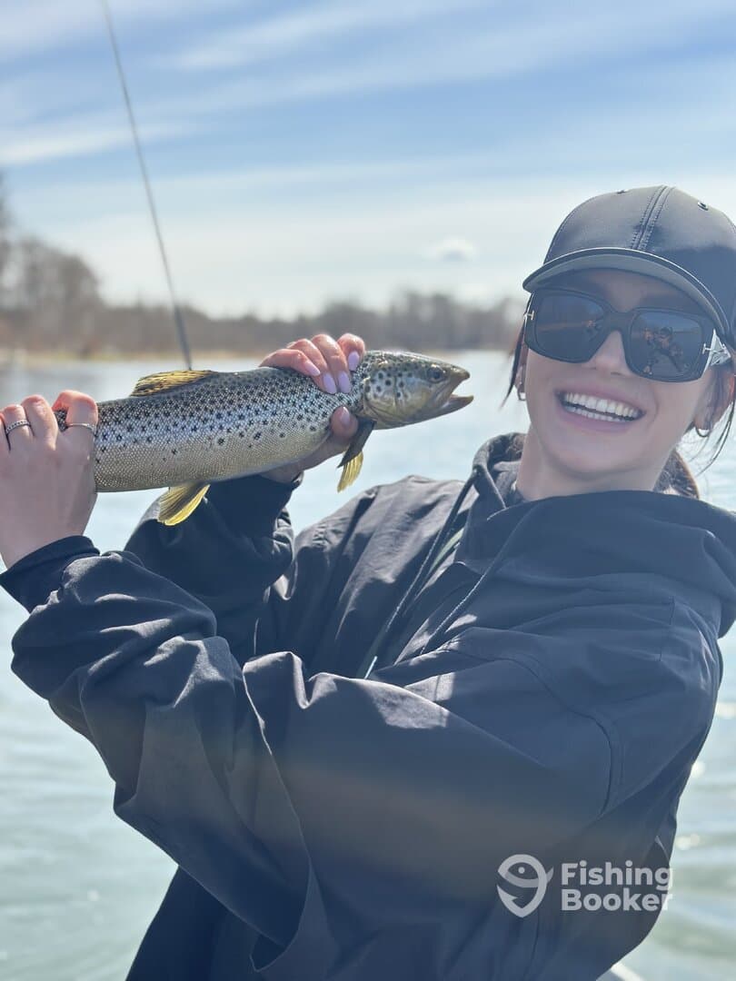 A smiling angler proudly displaying a large Brown Trout while fishing on a sunny day.