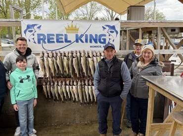 A family proudly poses in front of a catch board displaying an impressive haul of Walleye at Reel King in Monroe, Michigan.