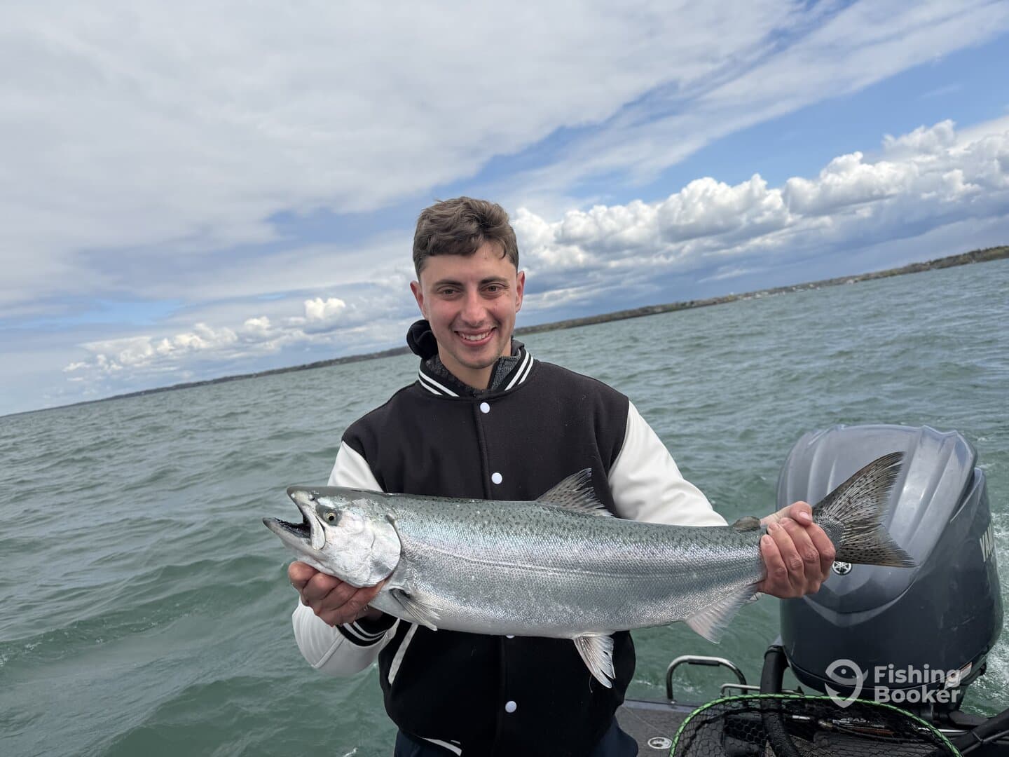 Young angler proudly holding a large Salmon while fishing on a boat, showcasing a successful catch in a scenic waterway.
