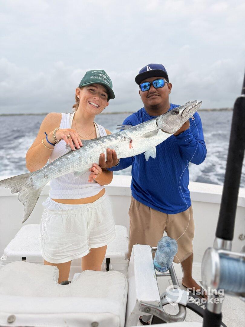 Two anglers proudly displaying a large Barracuda while on a fishing charter, showcasing a successful day on the water.