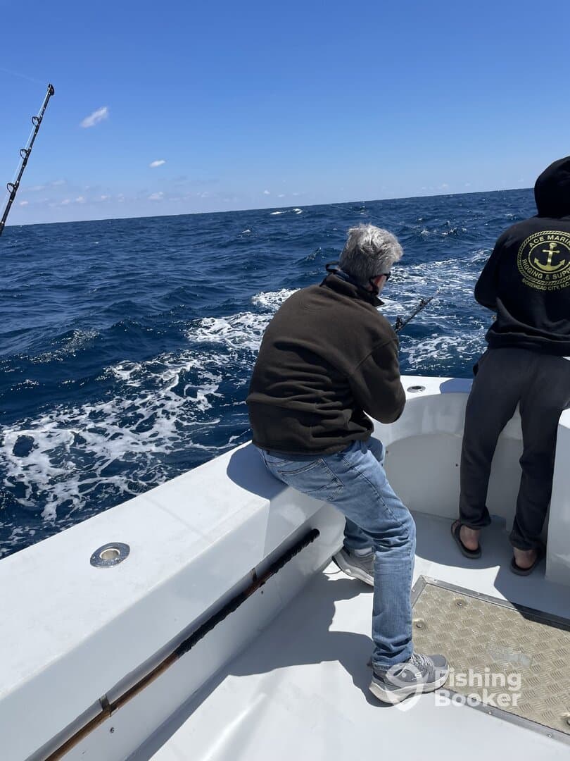 Two anglers engaged in fishing on a charter boat, with one reeling in a catch while enjoying a day on the open water.