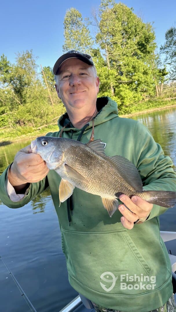 An angler proudly displaying a large freshwater fish while fishing on a serene river.