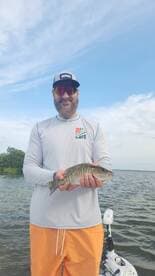 Angler proudly displaying a freshly caught striped bass while fishing on a calm waterway.