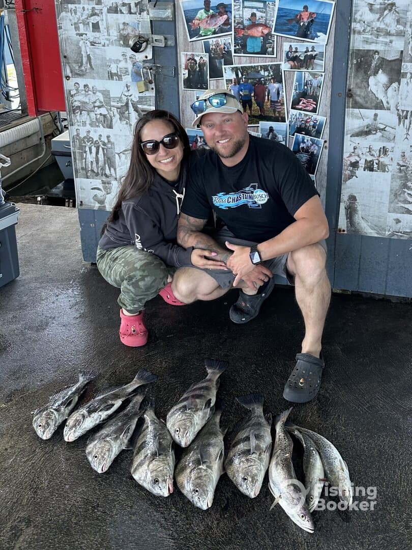 A couple proudly displaying their catch of several Black Drum and Speckled Trout at the dock, showcasing a successful fishing trip.