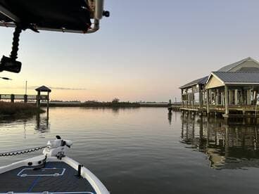 A serene view of a boat at dusk, showcasing a calm waterway and a dockside structure, perfect for fishing adventures.