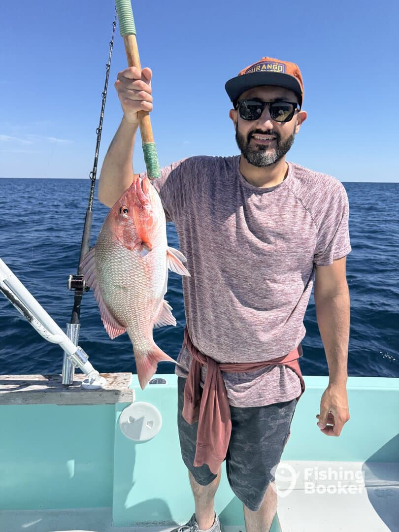 Angler proudly displaying a large Red Snapper while fishing offshore, showcasing a successful day on the water.