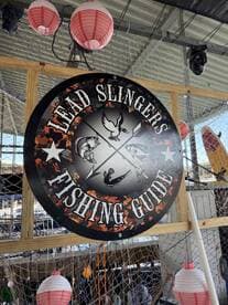 A decorative sign for 'Lead Slingers Fishing Guide' displayed in a fishing environment, surrounded by fishing gear and lanterns.