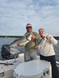 Two anglers proudly displaying their striped bass while fishing on a boat, showcasing a successful day on the water.