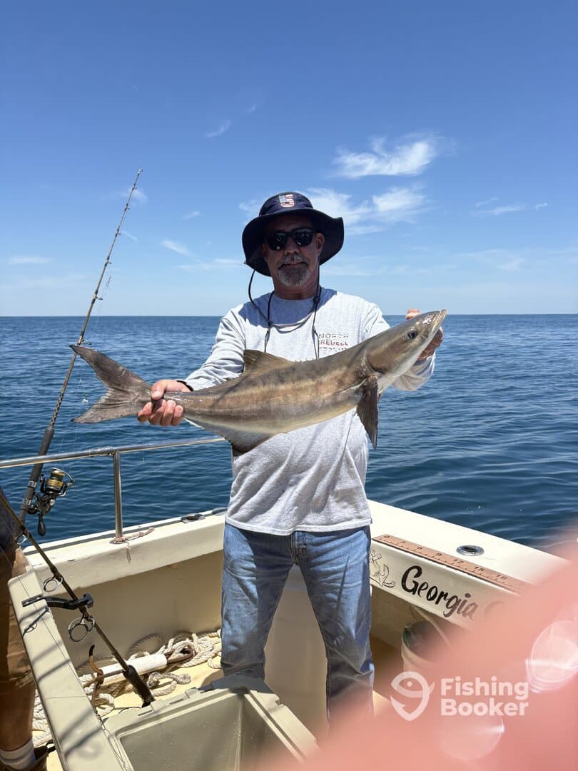 Angler proudly displaying a large shark while fishing on a boat in open water.