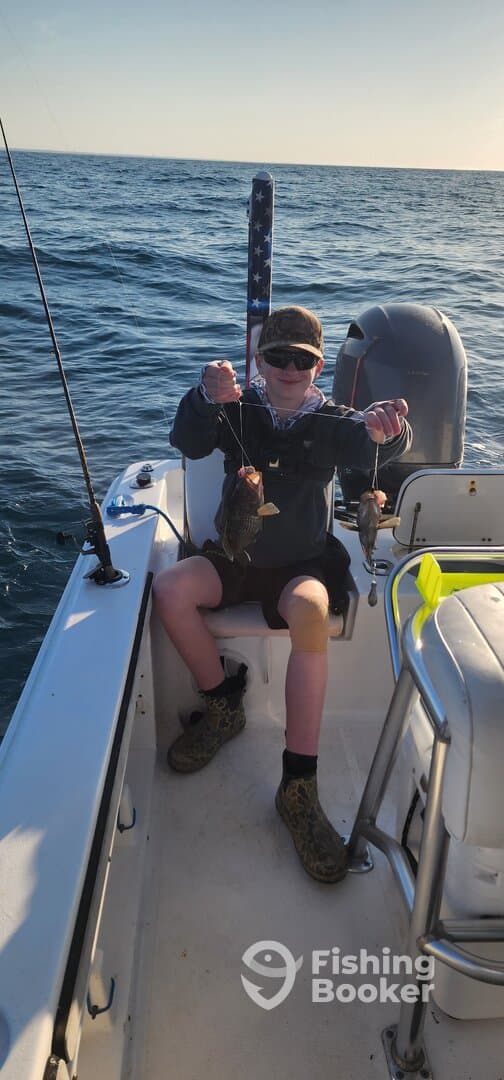 A young angler proudly displaying two caught fish while fishing on a boat, showcasing a successful day on the water.