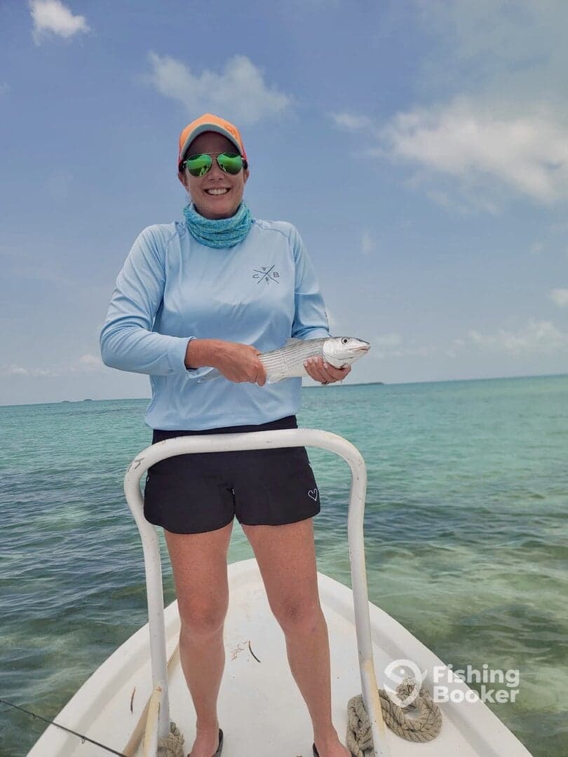 Angler proudly displaying a freshly caught fish while standing on a boat in clear waters, showcasing a vibrant fishing environment.